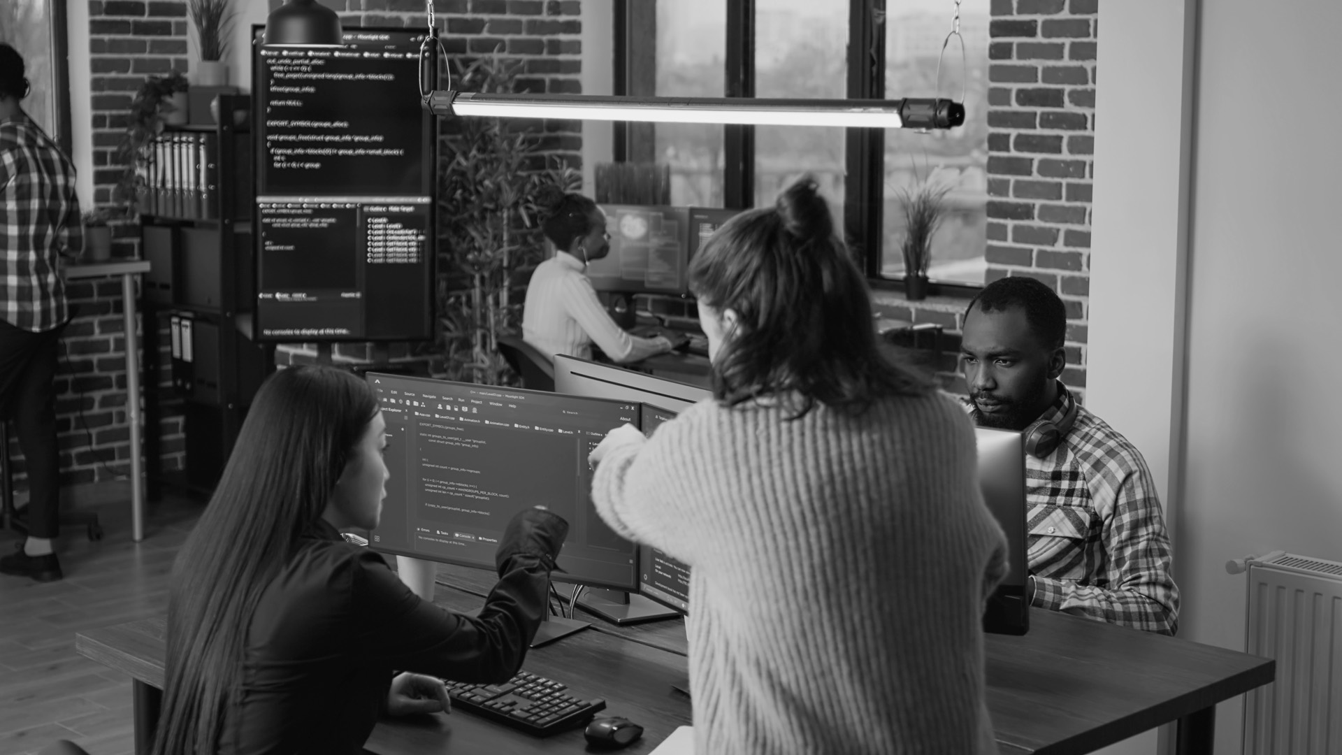 Trois personnes discutent devant un poste de développement, dans un espace de travail ouvert
